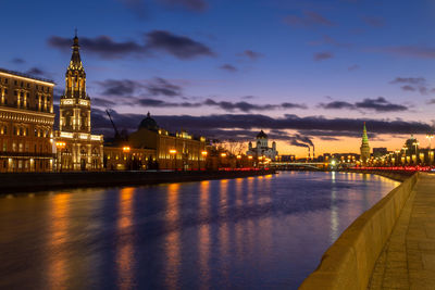 Illuminated buildings by river against sky in city