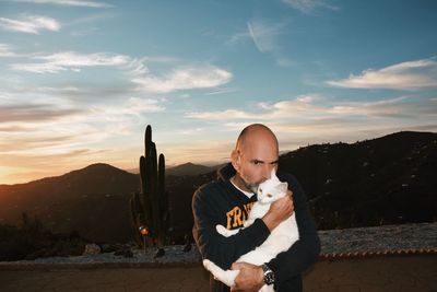 Man kissing cat while standing against sky