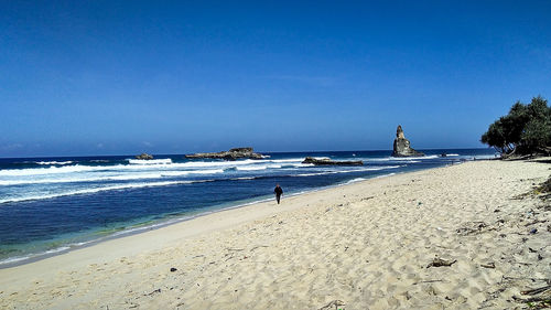 Man walking at beach against blue sky