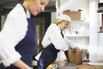 Young female baker working with colleague in commercial kitchen
