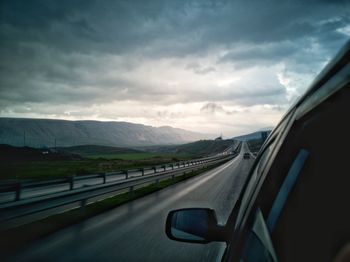 Car moving on road against cloudy sky