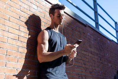 Young man using mobile phone against brick wall