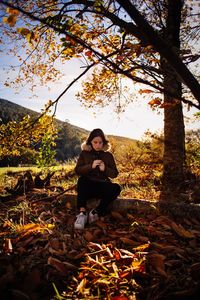 Young woman sitting on tree against sky