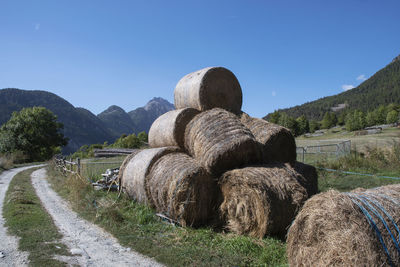 Hay bales on field by road against sky