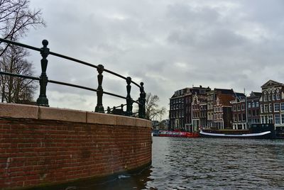 Canal by buildings in city against sky