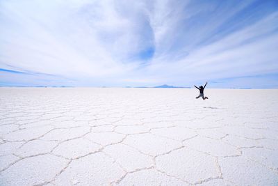 Full length of woman jumping at salt desert against sky