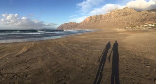 Shadow of man and woman at beach against sky