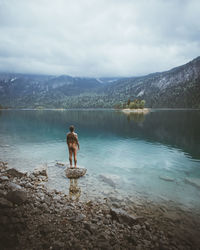 Rear view of shirtless man standing on lake against sky