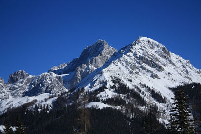 Low angle view of snowcapped mountains against clear blue sky