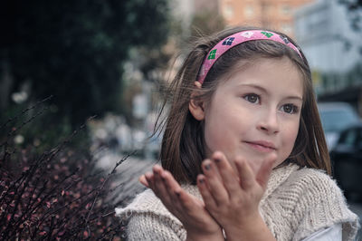 Close-up of thoughtful girl standing with hands cupped by plants on sidewalk