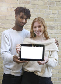 Portrait of young couple holding hands against wall