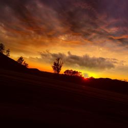 Scenic view of silhouette field against cloudy sky during sunset