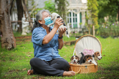 Senior woman wearing mask holding puppies sitting outdoors