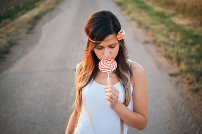Young woman eating lollipop while standing on road