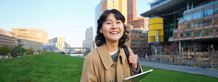 Portrait of young woman standing against buildings