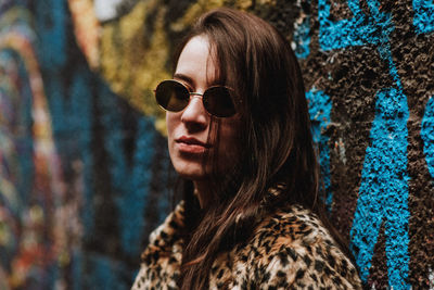 Portrait of young woman wearing sunglasses against graffiti wall