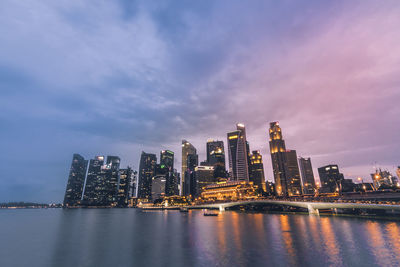 Illuminated buildings by river against sky in city