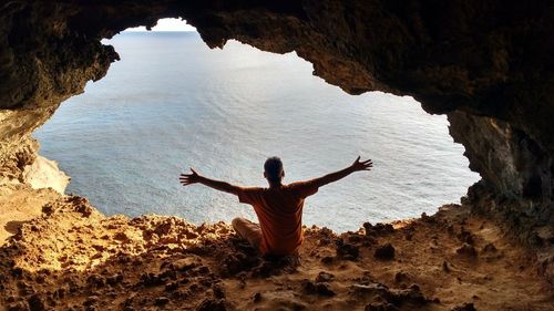 Rear view of man standing on rock formation against sea