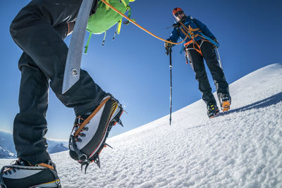 A female mountaineer in cramp-ons leads the way down a glacier.