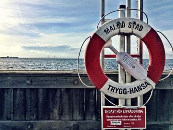 Road sign by pole against sea