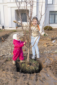 Happy smiling woman plants an apple tree with her little daughter in the garden on sunny autumn day