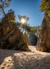 Low angle view of sunburst, rock formations on beach 