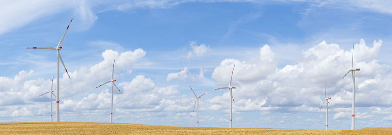 Large panorama of wind turbines with blue sky and white clouds in the background