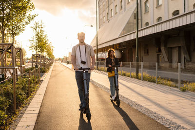 Man and woman riding electric push scooters on road in city during summer