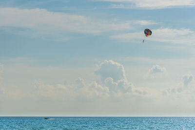 Distant view of person parasailing over sea against cloudy sky