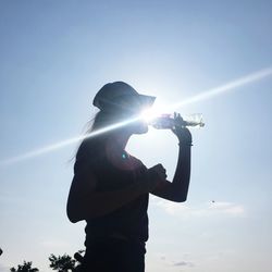 Silhouette woman drinking water while standing against sky on sunny day