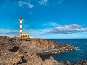 Lighthouse on rock by sea against blue sky