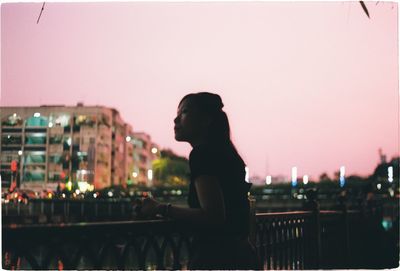 Side view of woman looking at cityscape against sky during sunset
