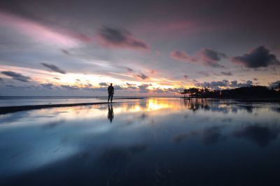 Silhouette man standing on shore at beach against sky during sunset