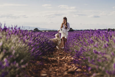 Woman with dog by purple flowering plants on land