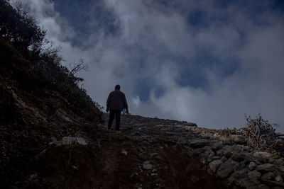 Rear view of man standing on rock against sky