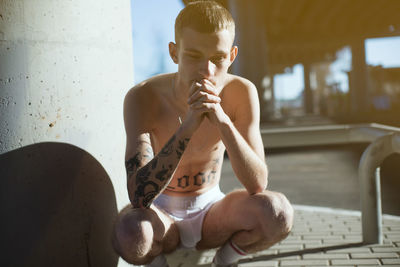 Thoughtful shirtless young man crouching outdoors