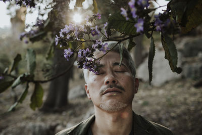 Mature man with eyes closed below blossoming tree in garden