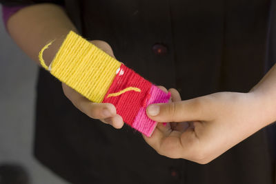 Cropped hands of boy holding strip with woolen strings