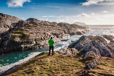 Rear view of woman standing on rock by sea against sky