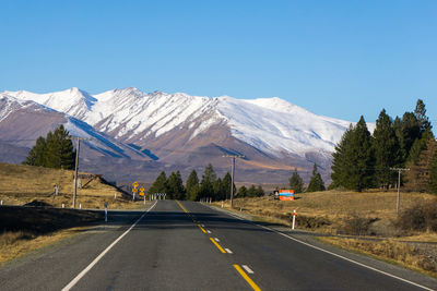Road leading towards snowcapped mountains against clear blue sky