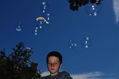 Low angle view of boy with bubbles in mid-air against blue sky