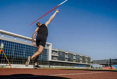 Man with arms raised against clear blue sky