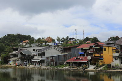 Houses by river and buildings against sky