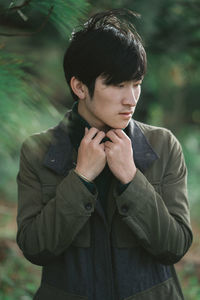 Young man looking away while standing on grass against trees