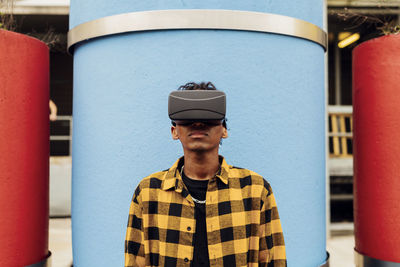 Man wearing virtual reality simulator standing in front of blue concrete pipe