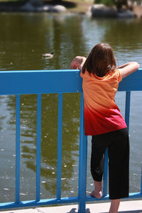 Rear view of girl leaning on railing against river