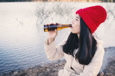 Young woman drinking beer at lakeshore