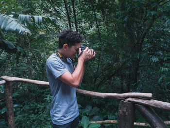 Man holding camera while standing by tree in forest