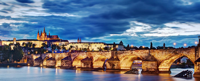 Arch bridge over river against buildings in city at night