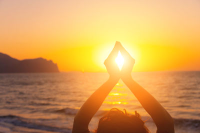 Young woman raises her hands, praying in the light of sunset or sunrise. silhouette of female hands